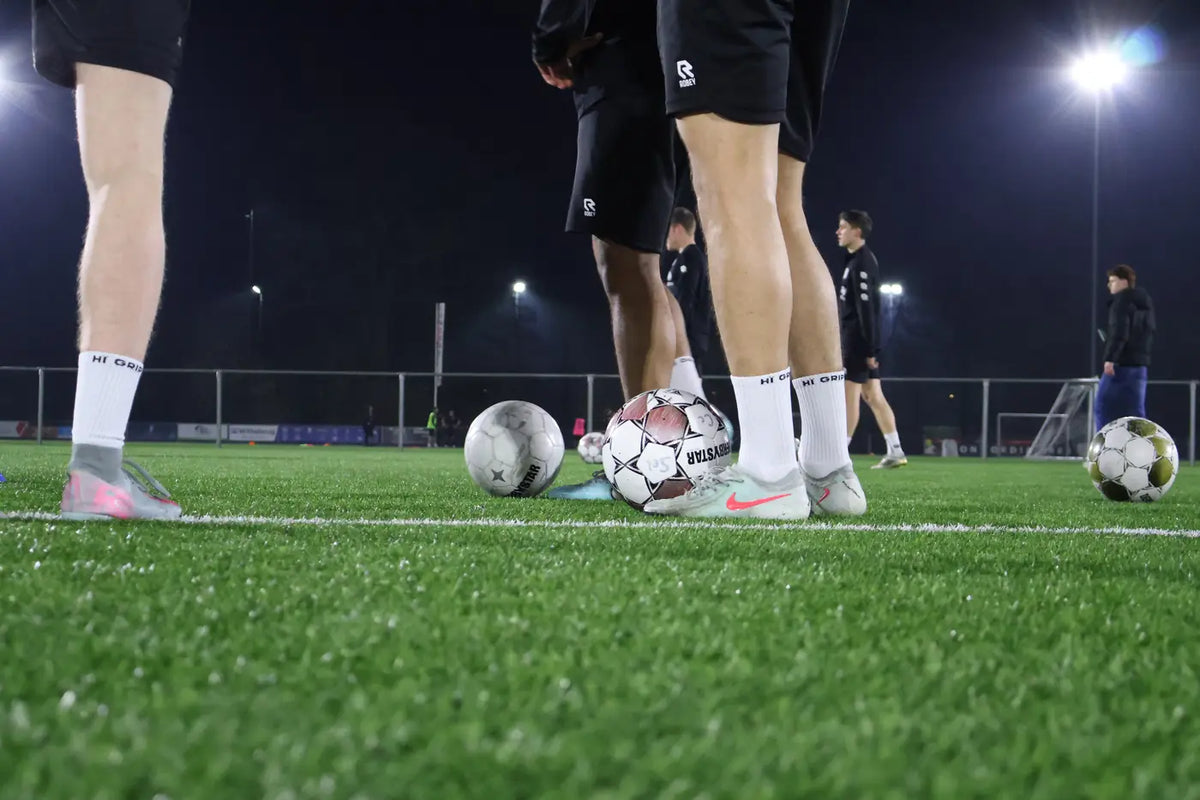 Spelers met ballen op het veld onder de lichtmasten