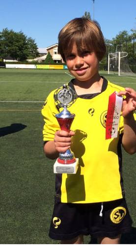 Founder as a child holding a trophy on the football pitch