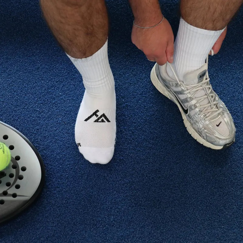 Padelspeler strikt zijn schoen, witte gripsokken op een blauwe baan