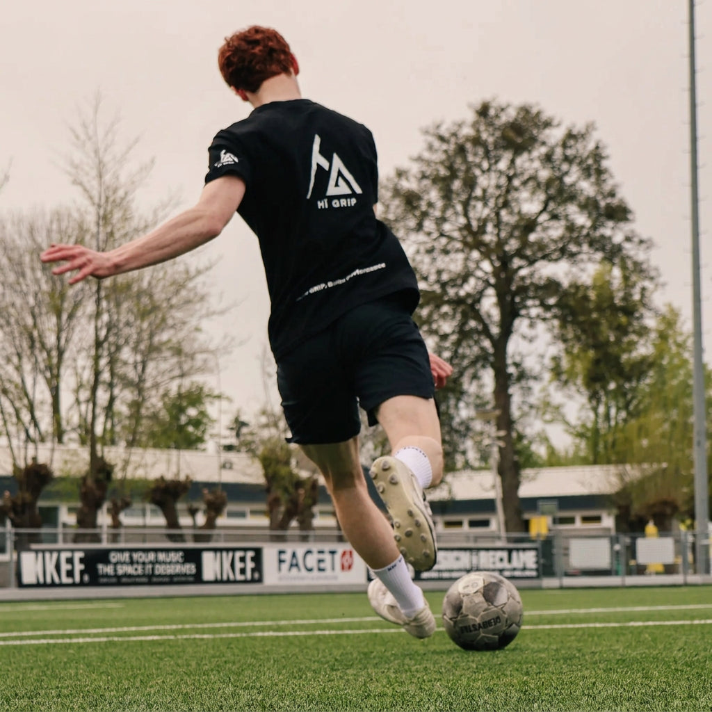 Voetballer in HÏ Grip-shirt haalt uit op een kunstgrasveld